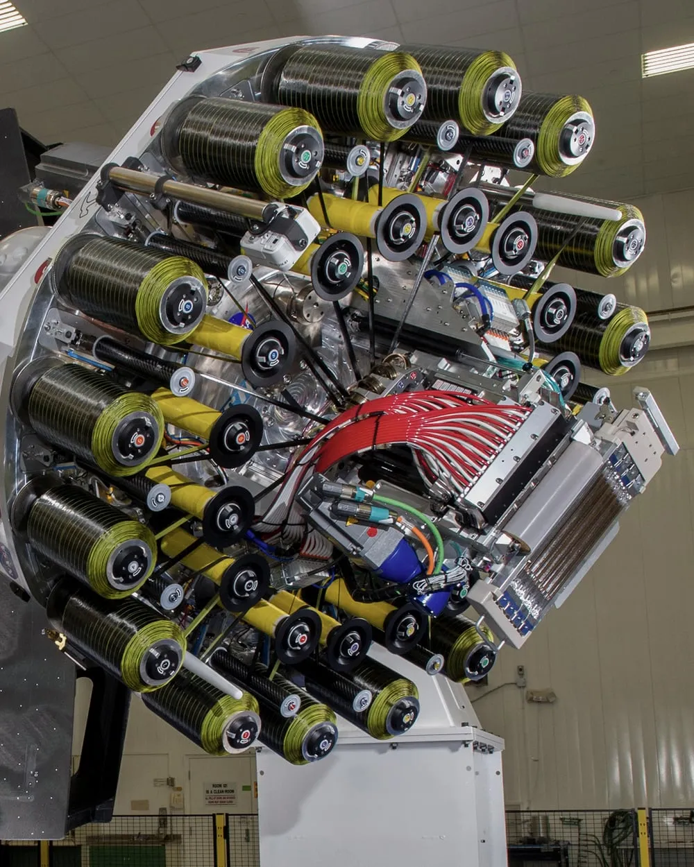 Close view of a robotic fiber placement end effector, its tow spools and servo drives arranged around the compaction roller.