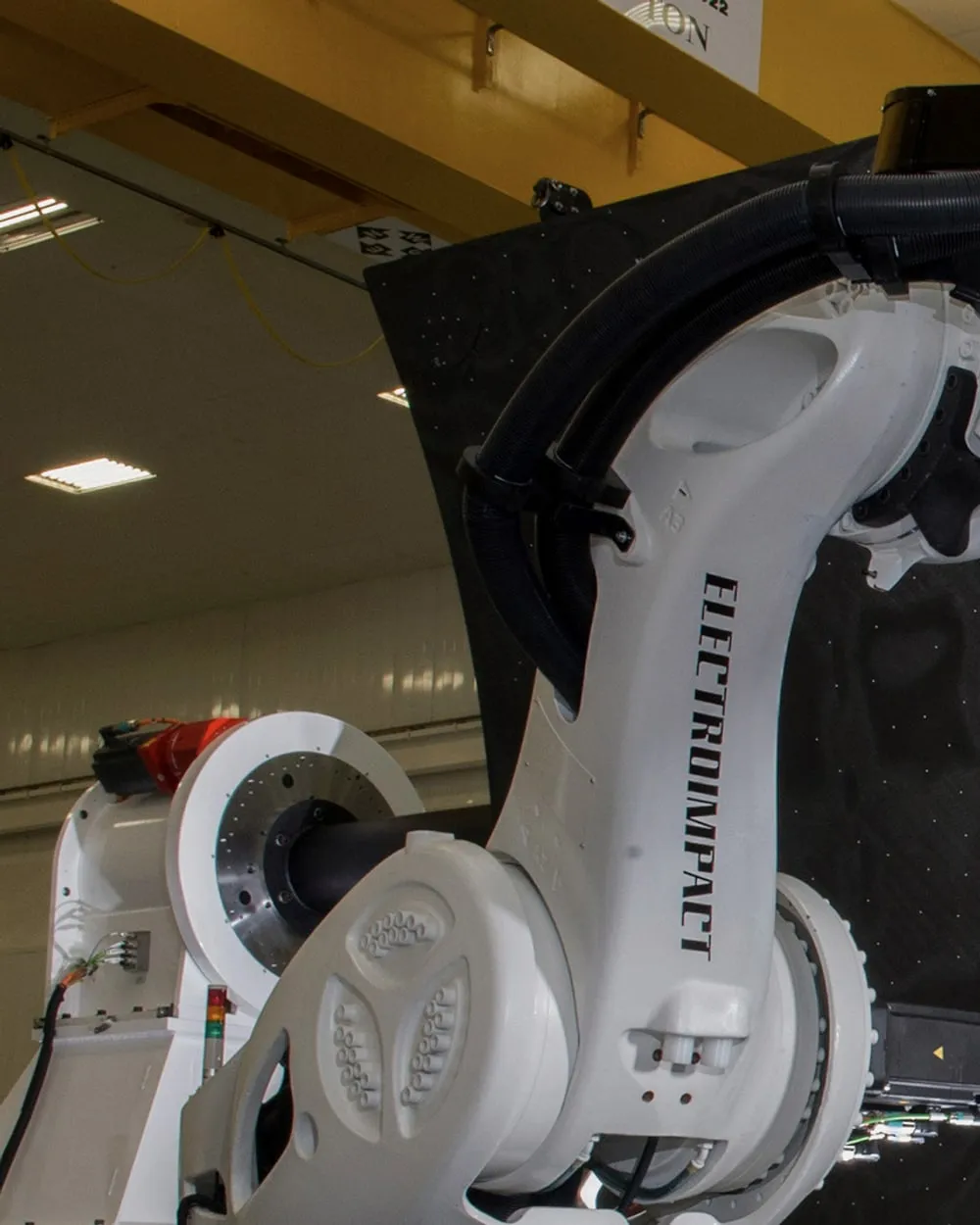 An articulated industrial robot arm, its cable loom routed along the upper arm casting, working against a dark composite panel.